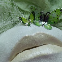 Mundabformung in Vollguss, im Objektrahmen angebracht, verziert mit strukturiertem Seidenpapier, Satinband, Perlen-Rosenborte sowie Schmetterlingen.